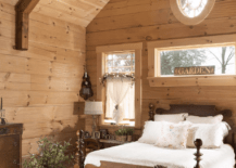 log home bedroom with white bedding ruffle bedskirt oval window wood paneling four poster bed wood