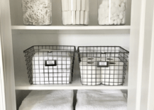 white linen closet in bathroom with white folded towels wire baskets with toilet paper soap apothecary jars q-tips cotton swabs