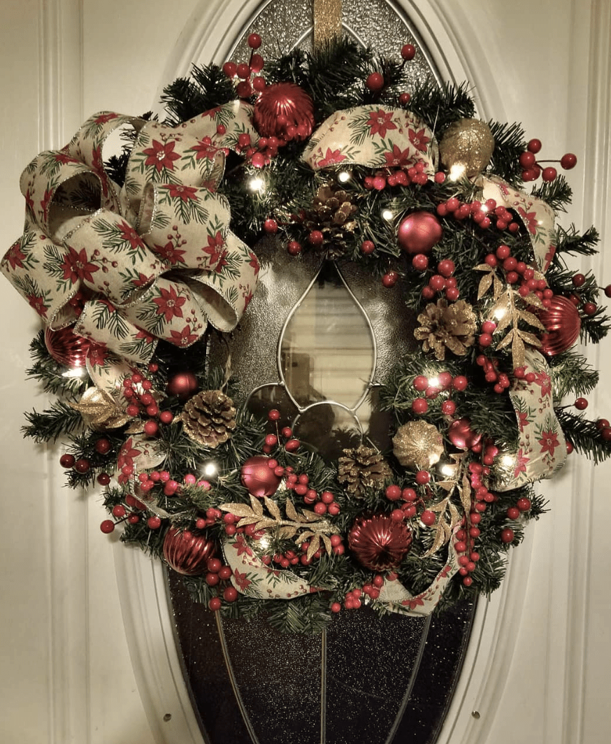 lit up christmas wreath on front door with holly berries and pinecone accents