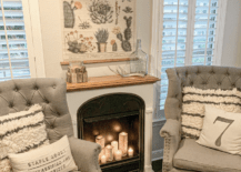 White room with small fireplace with candles inside grey tufted chairs with farmhouse pillows