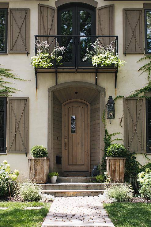 Juliet balcony over a front wood plank door in a cottage home fitted with vintage shutters and climbing ivy.