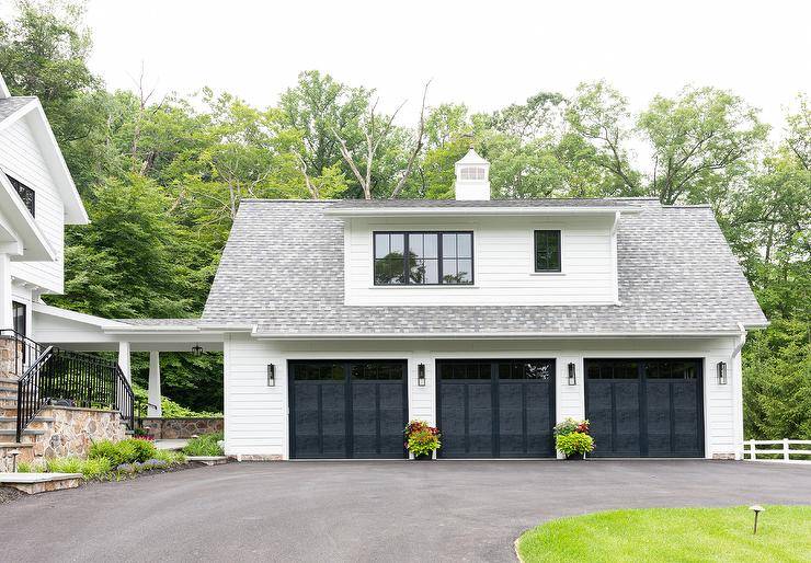 A freestanding 3 car garage finished with white siding is contrasted with black garage doors.