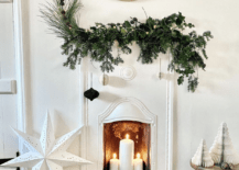 all white room with tiny white fireplace with greenery on mantle fireplace candles with white star and christmas trees