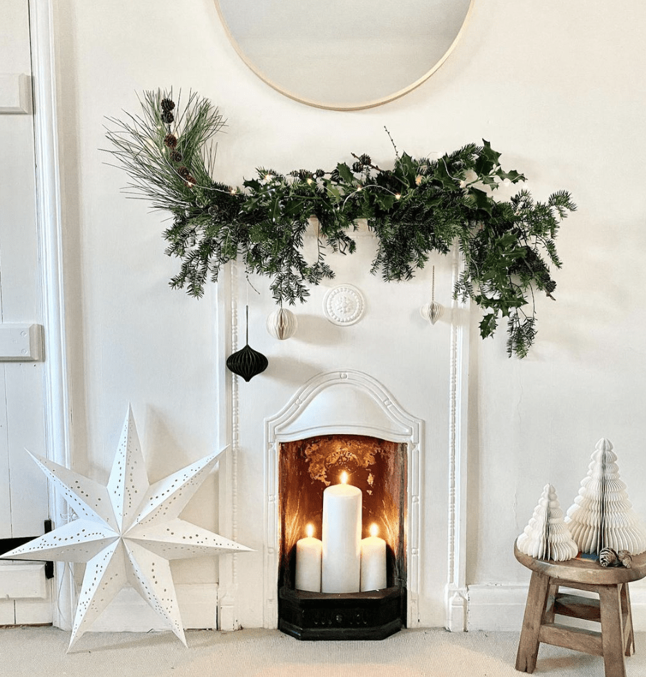 all white room with tiny white fireplace with greenery on mantle fireplace candles with white star and christmas trees