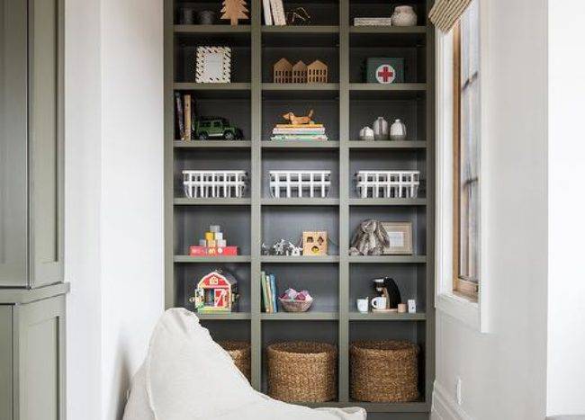 Floor to ceiling green built-in toy shelf decorated and styled with knick-knacks and woven storage bins for an organized appeal.