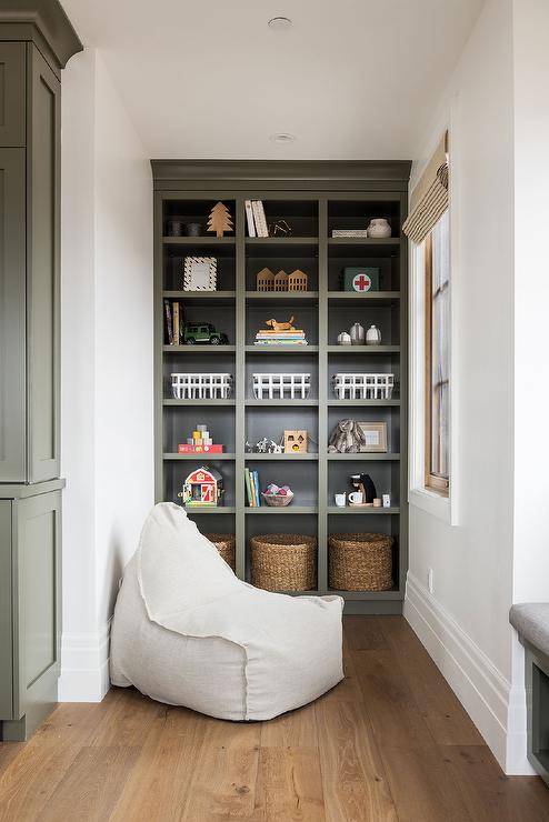 Floor to ceiling green built-in toy shelf decorated and styled with knick-knacks and woven storage bins for an organized appeal.