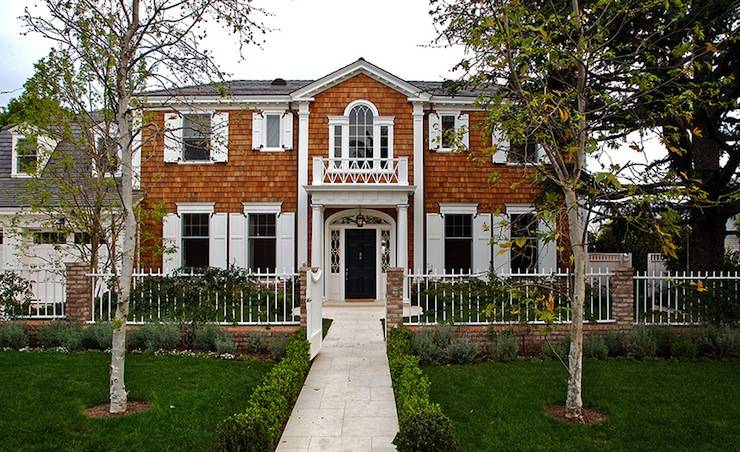 Gorgeous Colonial style home with cedar shingle siding and slate tiled roof. The windows are dressed with white shutters and the black front door framed by a portico and sidelights. A brick and white iron fence complete the homes exterior with lush boxwood hedges and a flagstone pathway leading to the entry.