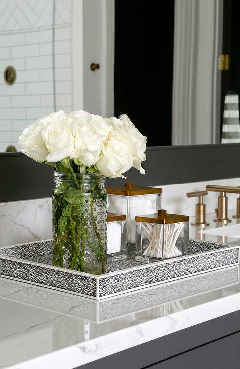 A black and white shagreen tray sits atop a white quartz countertop accenting a black washstand positioned beneath a black framed vanity mirror.