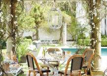 Amazing garden with pergola accented with a white lantern illuminating a round bistro table lined with French bistro chairs.