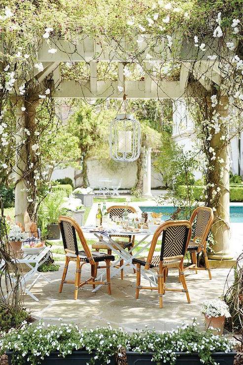 Amazing garden with pergola accented with a white lantern illuminating a round bistro table lined with French bistro chairs.
