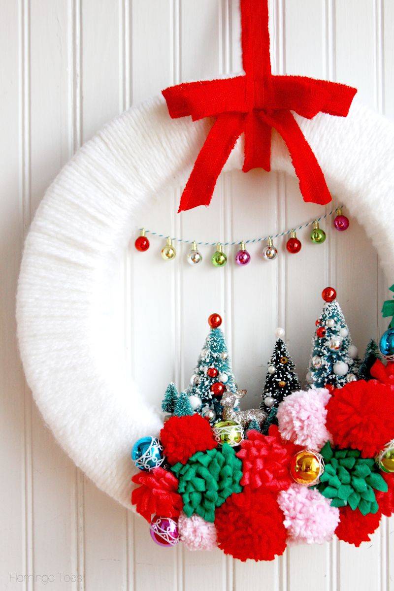 white yarn wrapped wreath with retro decorations red ribbon pom poms and bottle brush trees