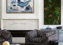 Contemporary living room features modern black and white lounge chairs on a black rug with white coffee table, abstract art over a marble look fireplace mantel and a living wall over a blue credenza.