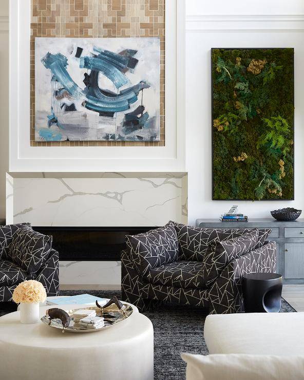 Contemporary living room features modern black and white lounge chairs on a black rug with white coffee table, abstract art over a marble look fireplace mantel and a living wall over a blue credenza.