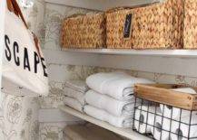 close up of interior of linen bathroom closet seagrass baskets hooks on wall wallpaper floral folded white towels