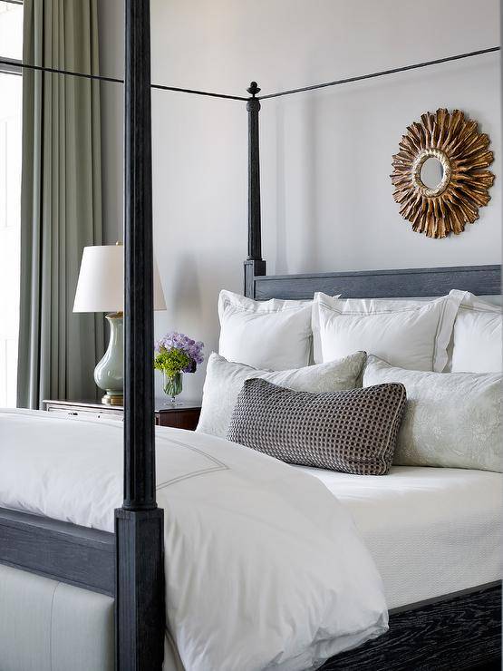 Bedroom features a small gold sunburst mirror over a black 4 poster bed with white bedding.