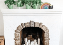 white fireplace with stone border arch white candles inside and green ،ted plants on mantle with rainbow and ، of gold