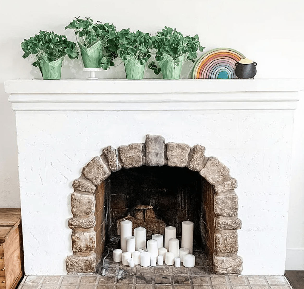 white fireplace with stone border arch white candles inside and green potted plants on mantle with rainbow and pot of gold