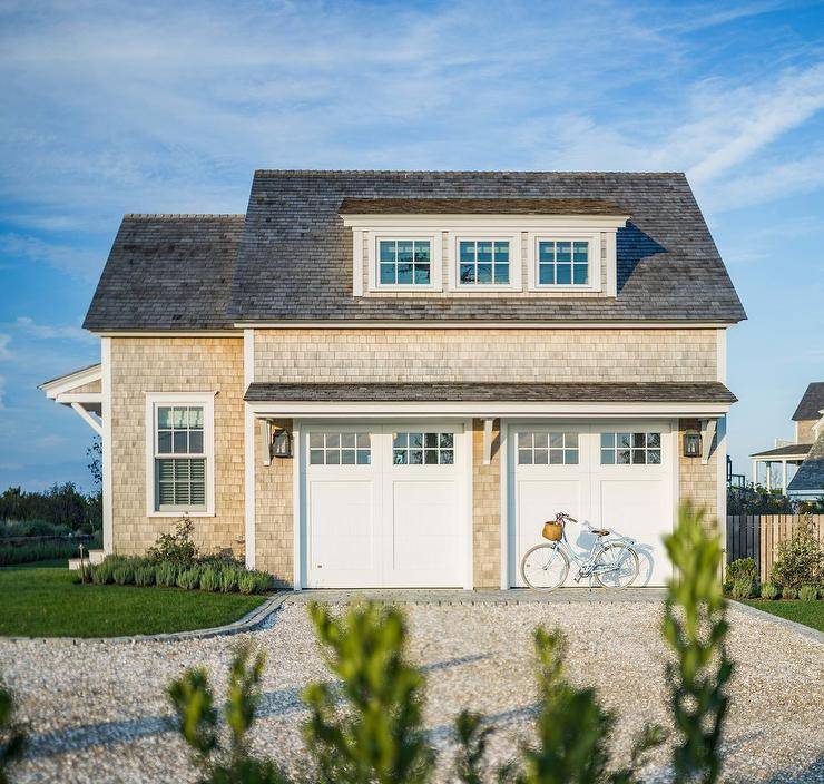 Gorgeous tan singled cottage home is accented with a gray shingled roof and boasts a gravel driveway leading to a 2 car garage.