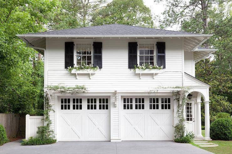 Gorgeous home exterior boasts a traditional two car garage framed by white siding and positioned under an above-garage apartment with two windows flanked by black shutters and fitted with white flower boxes.