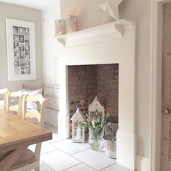 a large non-working fireplace with bricks inside, candle lanterns, flwoers and whitewashed baskets is chic