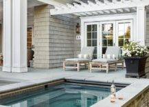 Rustic stone clad spa is accented with gray pool line tiles and positioned in front of two pool loungers with gray cushions topped with gray striped bolster pillows. The loungers sit beneath a white pergola.