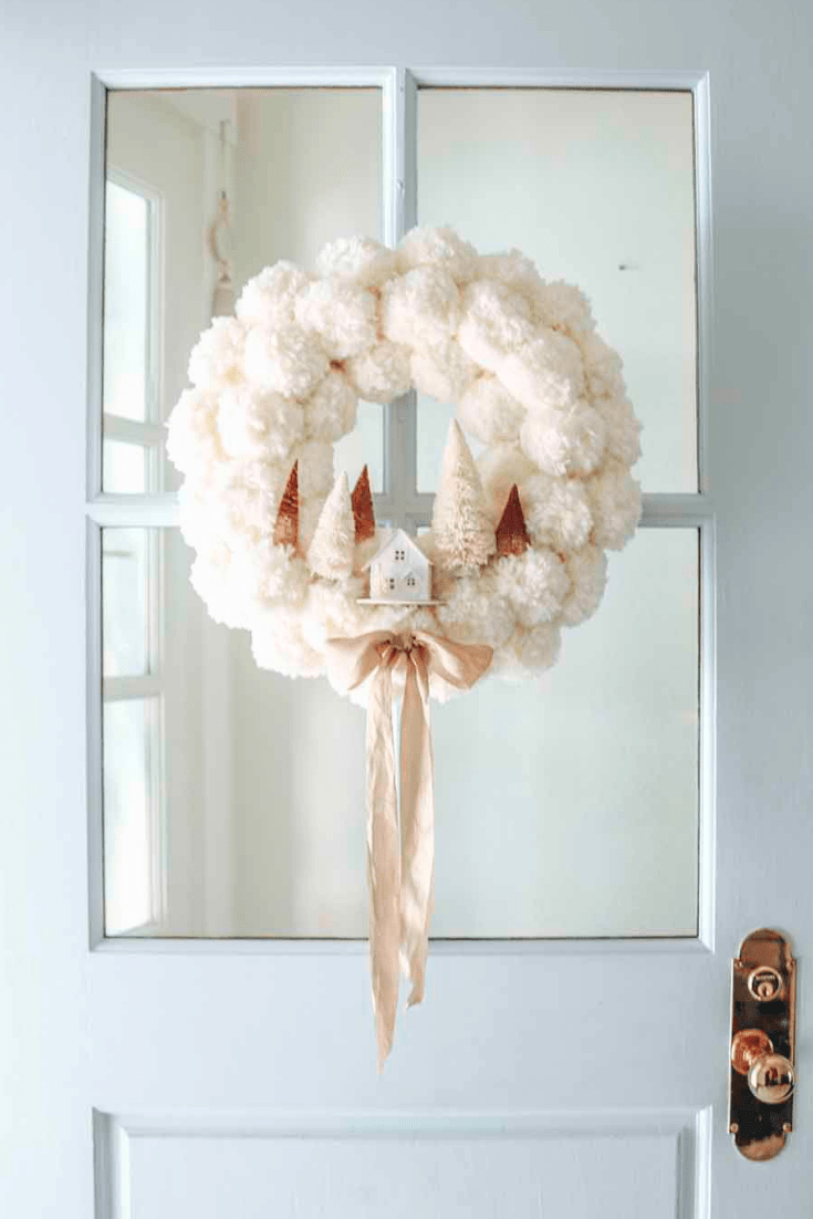 white pom pom christmas wreath with little white house and bottle brush trees