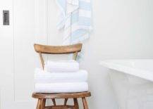 White and gray bathroom styled with a brown wooden vintage chair storing folded towels beside a white clawfoot tub atop large gray hexagon floor tiles.