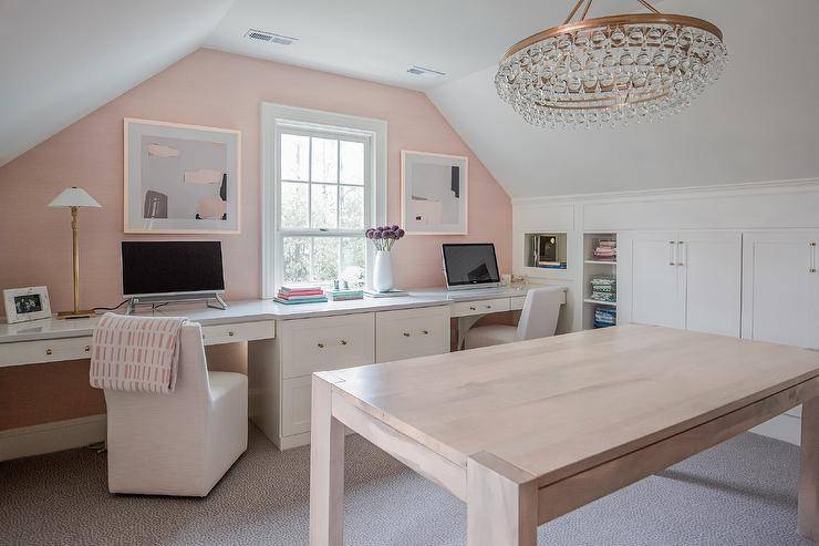 Spacious white and pink home office with pink walls features white built in desks with white slipper chairs and a brown lacquer table lit by a Robert Abbey bling chandelier.