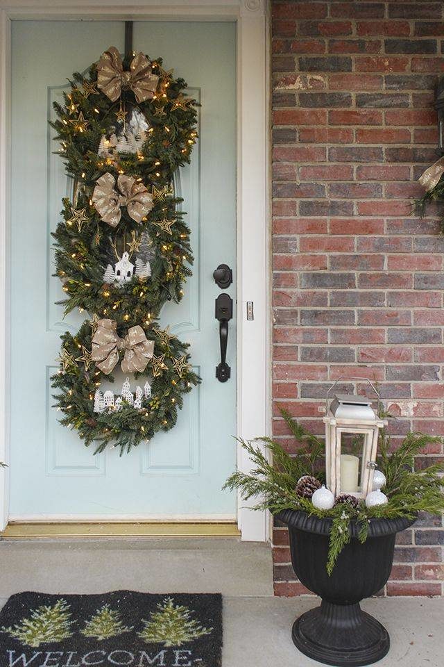 trio of three christmas wreaths hanging on light blue door with lights