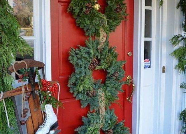 red front door with three evergreen Christmas wreaths and garland hanging old fashioned sled with skates