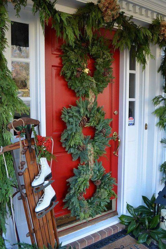 red front door with three evergreen Christmas wreaths and garland hanging old fashioned sled with skates