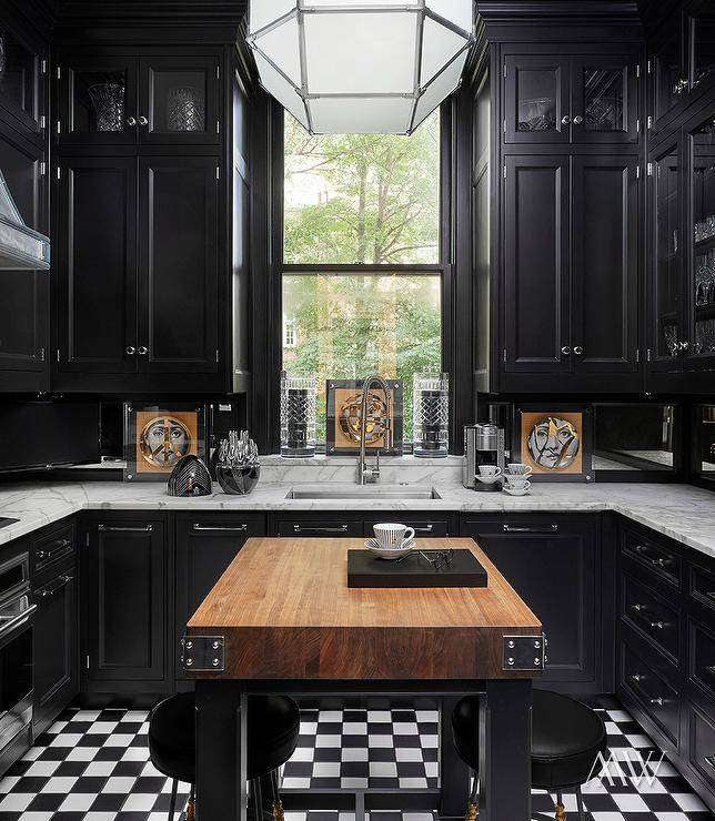 Stunning contemporary black and white kitchen features a butcher block freestanding island with black backless island stools, lit by a Suzanne Kasler Morris lantern and black and white checkered kitchen floor tiles.
