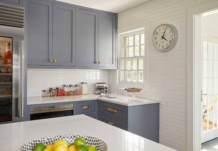 Blue-gray shaker kitchen cabinets are topped with a quartz countertop and complemented with vintage brass pulls.