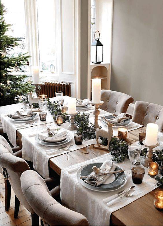 a chic winter tablescape with white runners, a dried eucalyptus runner, deer figurines, pillar candles