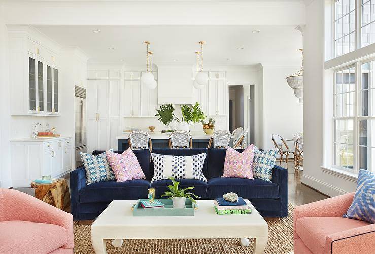 Contemporary living room furnished with a dark blue velvet sofa and pink swivel accent chairs surrounding a hoof coffee table on a jute rug.