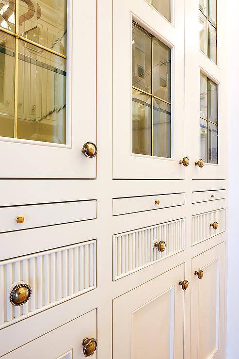 Brass beaded knobs accent white kitchen cabinets fixed under gold leaded glass cabinets.