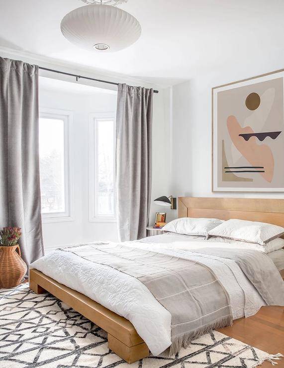 Bedroom features a tan wooden platform bed with pink and gray abstract art, gray curtains and a gray and white rug.