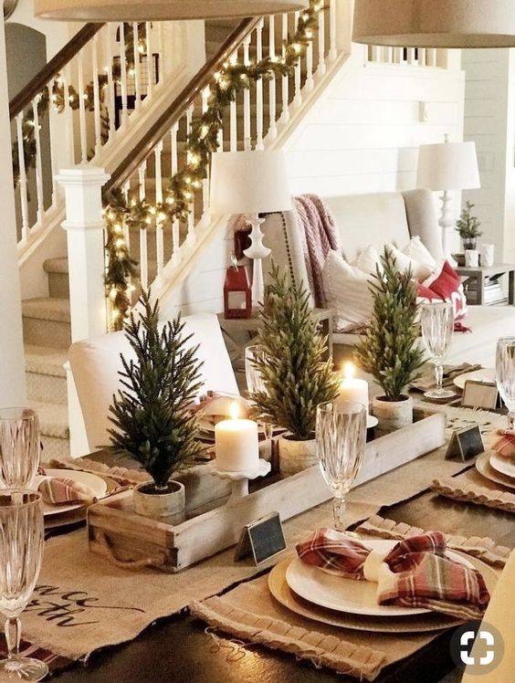 a homey winter table with a burlap runner and placemats, plaid napkins, mini Christmas trees, candles, plaid napkins