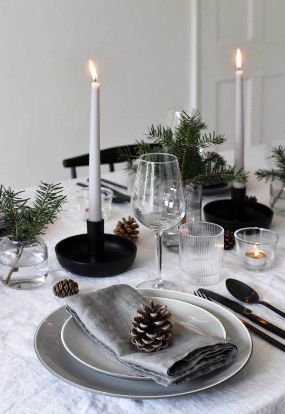 a Scandinavian winter tablescape with pinecones, evergreens, thin and tall candles and black candleholders