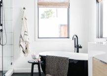 Black and white modern bathroom designed with a catty corner tub on black hexagon floor tiles and a matte black gooseneck tub filler.