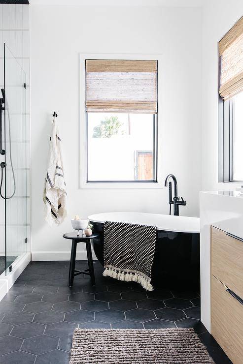 Black and white modern bathroom designed with a catty corner tub on black hexagon floor tiles and a matte black gooseneck tub filler.