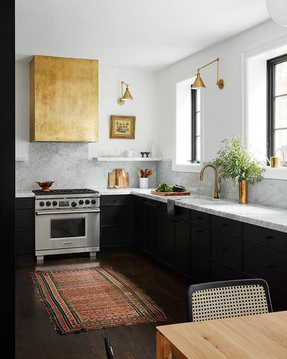 A brass dome range hood stands over a gray marble slab backsplash and a stainless steel Wolf range.