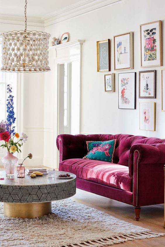room with burgundy velvet couch gold frames and round coffee table with glass bead chandelier
