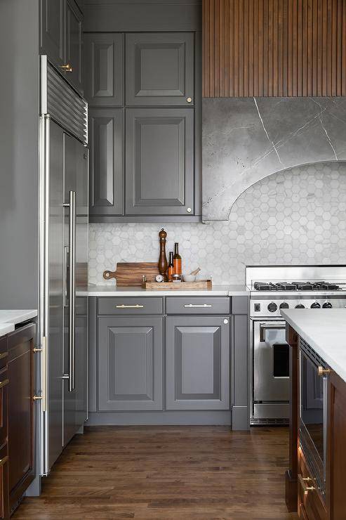 Kitchen features charcoal gray cabinets with a dark gray marble curved range hood over honed light gray hexagon marble backsplash tiles and reeded walls.