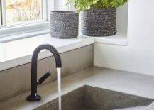 Under a window, an oil rubbed bronze gooseneck faucet is mounted to a concrete washstand countertop over a concrete trough sink.