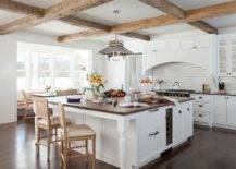 Rustic wood ceiling beams accent a kitchen boasting a large square white island with French turned legs seating tan French cane stools at a walnut butcher block top. The island is finished with oil rubbed bronze hardware and lit by a vintage metal lantern.