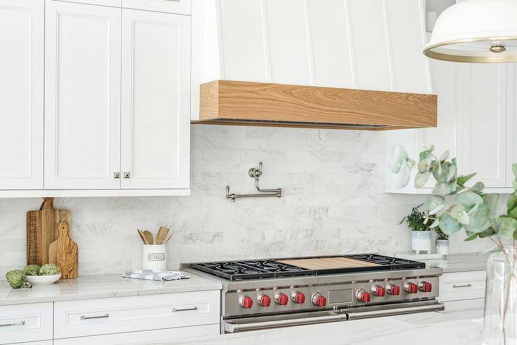 Bright kitchen boasts an oak trimmed white wooden range hood over a cooktop, gray subway wall tiles and a nickel swing arm pot filler.