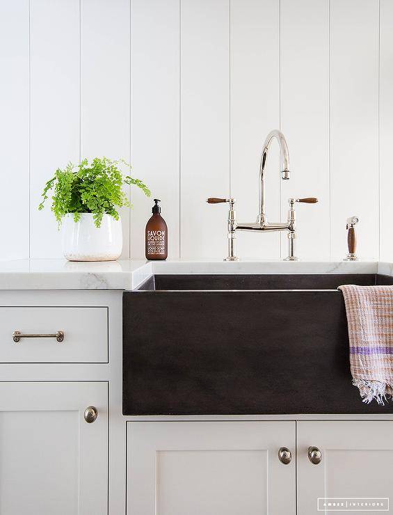 Cottage mudroom surrounded by vertical white shiplap walls and shaker cabinetry is contrasted by a black fireclay apron sink. Nickel hardware and a polished nickel faucet, add a luster to the simple airy furnishings while a marble countertop attracts the eye, revamping the mudroom into an elegant, streamlined design.