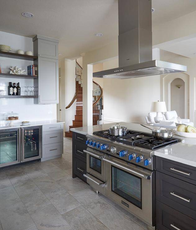 Traditional kitchen features a thermador island cooktop with double ovens under a range hood and a brown wooden island topped with white quartz.