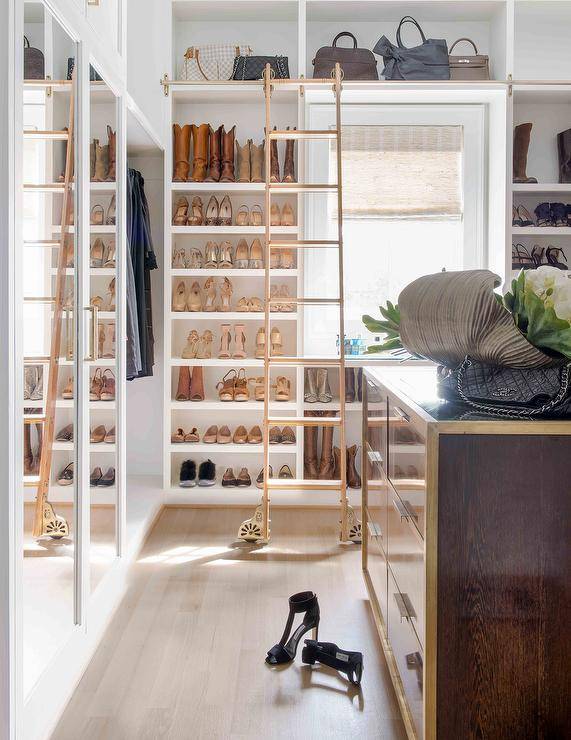 Walk-in closet boasting a ladder on rails styled with custom built-in shoe shelves and purse cubbies. This large <yoastmark class=